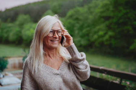 Senior woman standing terrace making phone call.