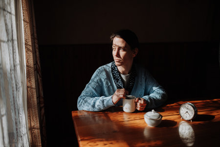 Portrait of poor despaired woman sitting at table drinking tea.