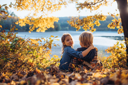 Siblings in autumn nature, sitting on fallen leaves.の写真素材