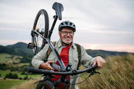 Smiling senior cyclist carrying bicycle on shoulder in nature.の写真素材