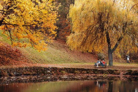Son and older father sitting on bench by lake and talking.