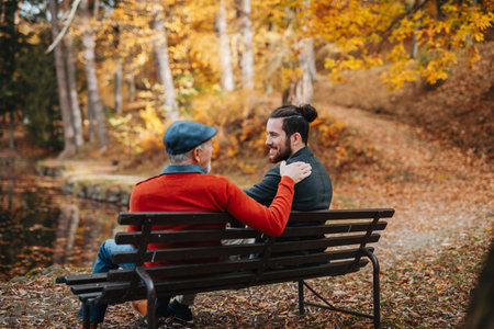 Son and older father sitting on bench by lake and talking.の写真素材