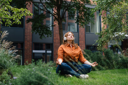 Beautiful mid size woman meditating in park, listening podcast.の写真素材