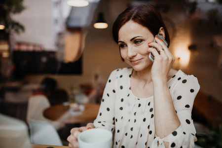 Redhead woman working remotely from coffee shop, making phone call.の写真素材
