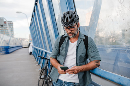 Bearded cyclist using phone while waiting for bus.の写真素材