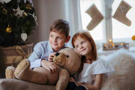 Small girl and boy indoors at home at Christmas, holding teddy bear.の写真素材