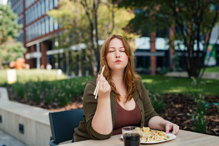 Plus size woman having lunch outdoors, eating noodles.の写真素材