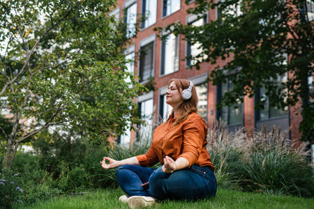 Beautiful mid size woman meditating in park, listening podcast.の写真素材