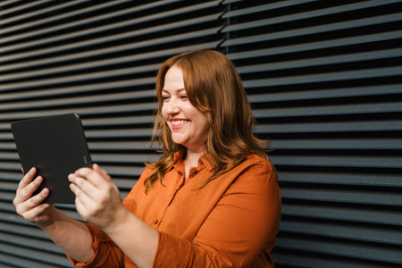 Curvy adult woman holding tablet, reading something.の写真素材