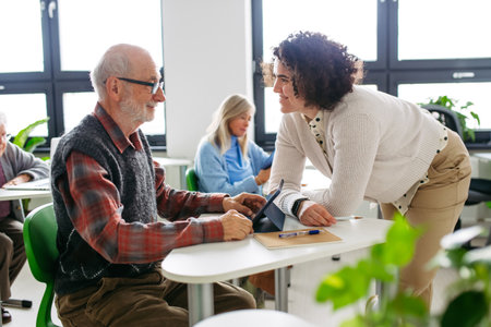 Senior man learning digital skills with tutor support in community center.の写真素材