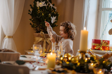 Cheerful small girl indoors at home at Christmas, looking at christmas ornament.の写真素材