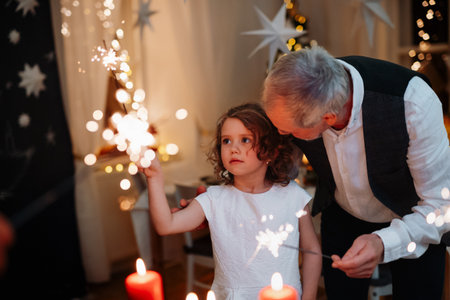 Grandfather and granddaughter holding sparklers during Christmas celebration.の写真素材