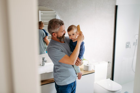 Morning routine in bathroom, father combing son hair.の写真素材