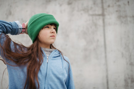 Outdoor portrait of cute young girl with beanie hat. Girl with long hair standing on playground in...