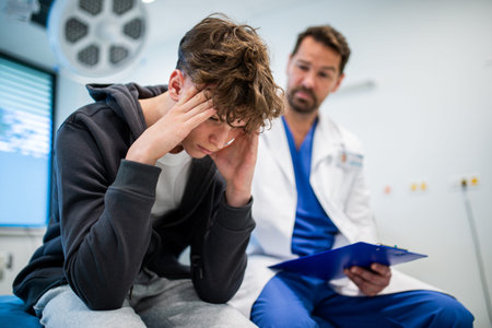 Depressed teenage patient sitting on hospital bed, talking with caring doctor.の写真素材