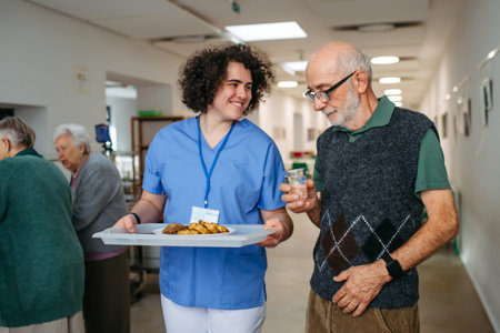 Senior man having lunch with supportive caregiver in community center cafeteria.の写真素材