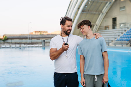 Coach giving advice to young swimmer, walking by pool.の写真素材
