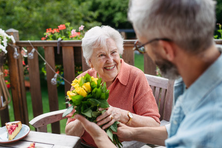 Portrait of mature son bringing bringing flowers to old mother.