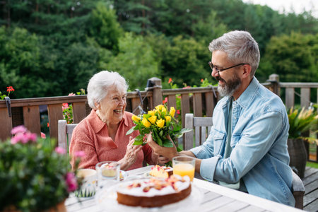 Portrait of mature son bringing bringing flowers to old mother.