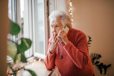 Old woman standing by window, making phone call.