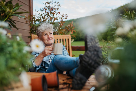 Senior woman with coffee sitting on terrace, resting after gardening.の写真素材