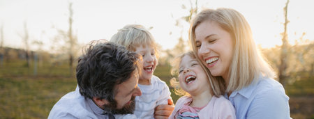 Spring portrait of parents with two small children on wlak in blooming orchard.