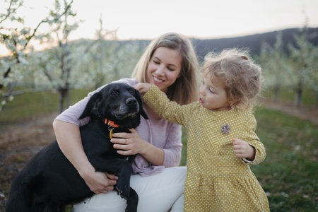 Girl with mother and dog in the middle of blooming orchard.
