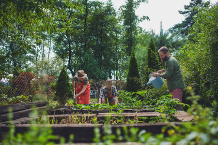 Happy young and old farmers working with garden tools outdoors at community garden.