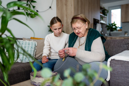 Elderly grandmother teaching girl knitting while spending time together.