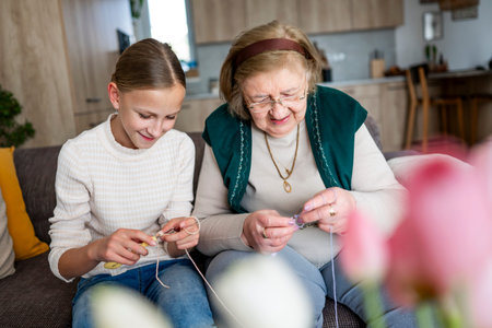 Elderly grandmother teaching girl knitting while spending time together.