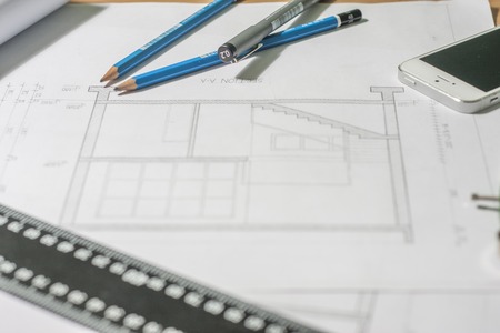 Architectural blueprints and blueprint rolls and a drawing instruments are set on the architects worktableの写真素材