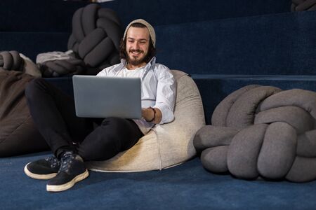 Caucasian man is working on a laptop in casual and relaxed office. Freelancer working at coworking space.の写真素材