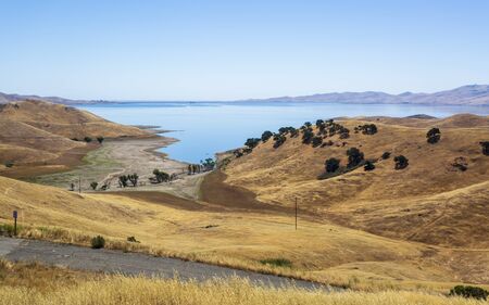 Driving through the golden hills of California the San Luis Reservoir State Recreation area sign and dam on the right side of the roadの写真素材