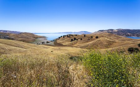 Driving through the golden hills of California the San Luis Reservoir State Recreation area sign and dam on the right side of the roadの写真素材