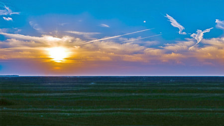 Sunset over a field with green grass and clouds in the skyの素材