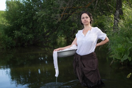 peasant woman washes clothes in the river near the forest