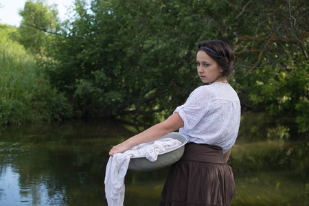 peasant woman washes clothes in the river near the forestの写真素材