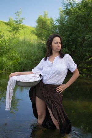 peasant woman washes clothes in the river near the forestの写真素材