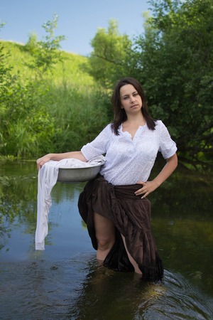 peasant woman washes clothes in the river near the forestの写真素材