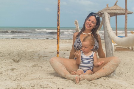 child with her mother playing on the beach of the ocean and the poolの写真素材