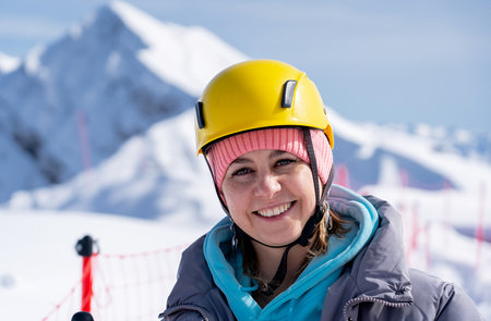 A girl in a yellow helmet stands against the backdrop of large white mountainsの写真素材
