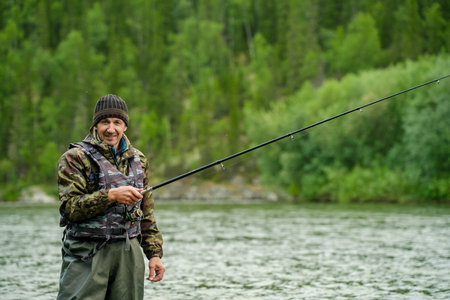 Fisherman with a fishing rod on a river against the background of a forestの写真素材