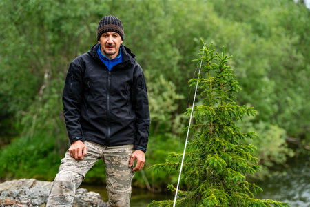 A male fisherman stands with a fishing rod near a spruce treeの写真素材