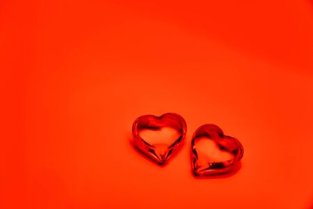Two transparent glass hearts on a bright red background.の写真素材
