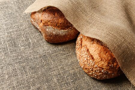 Two loaves of rustic bread lie on a burlap buried in a cloth of burlap with pestle for text. The...