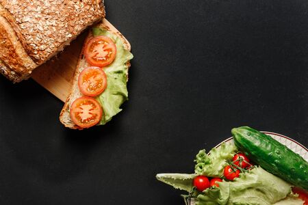 Flat lay composition with a sandwich, bread, lettuce. tomatoes and cucumber on a black background with space for text.の写真素材
