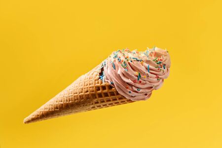 Ice cream in a waffle cone isolated on a bright yellow background. Marshmallow cake in a waffle cone. Falling cake colored with colored sugar sprinkles.の写真素材