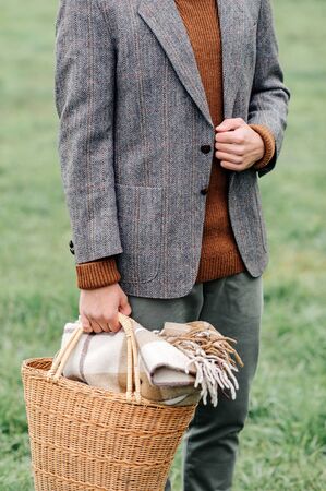 a man standing on the background of meadow grass, holds in his hand a picnic basket.の写真素材