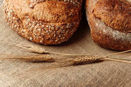 Two loaves of homemade bread on a burlap with ears of wheat.
