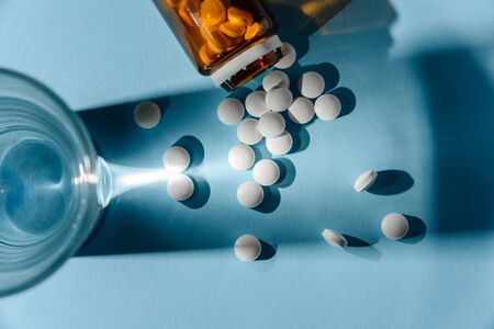 Flat lay composition with pills spilled out of a glass vial next to a glass of water. The concept of modern medicine.の写真素材